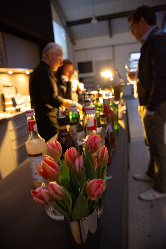 A bouquet of flowers in the foreground, in the background a barkeep mixing cocktails at a company event.
